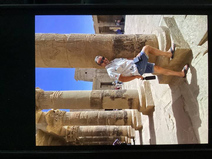 Tourist leans playfully against carved sandstone columns in Philae Temple.