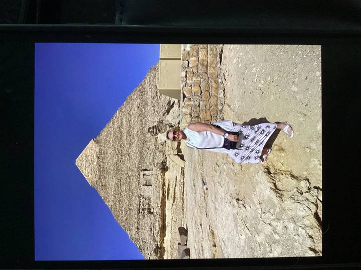 Woman stands smiling in front of a towering pyramid under a deep blue sky.