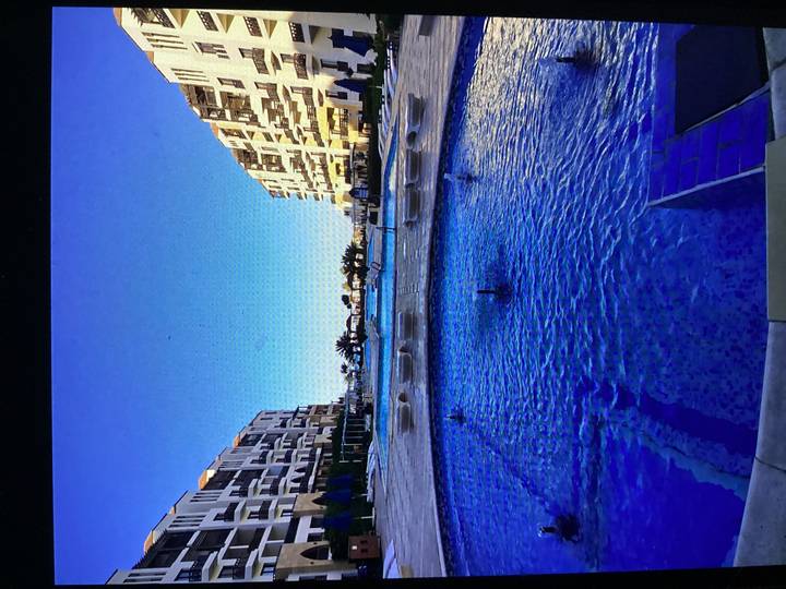 Modern seaside resort with blue fountain pool leading to distant swimming pools at sunset.