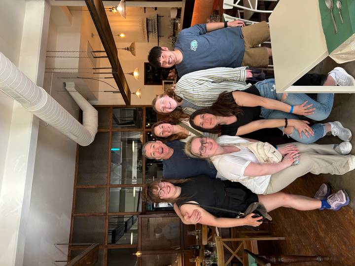 Indoor group photo of travellers posing with a smiling chef inside a modern restaurant.