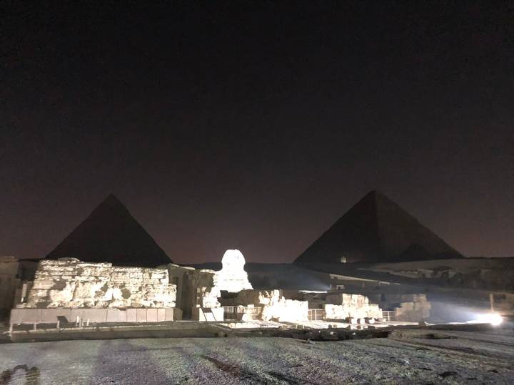 Nighttime view of the Sphinx and two pyramids faintly lit against a dark sky.