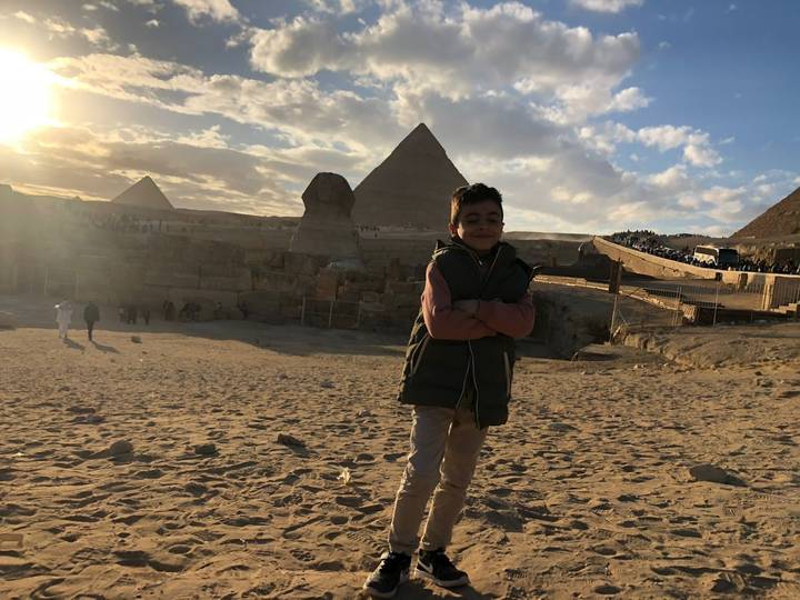 Child stands confidently with arms crossed before the Sphinx and pyramids at sunset.