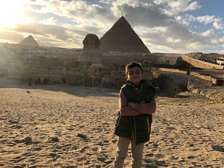 Boy poses before the Sphinx with pyramids and hazy sunlit sky in the background.