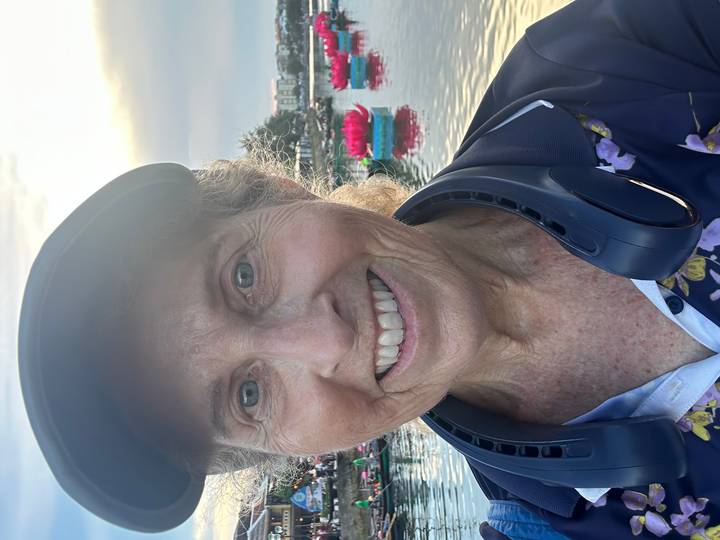 Close-up portrait of a smiling older traveller beside a lake filled with decorative pink lotus boats at sunset.