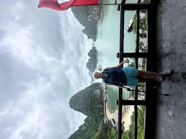 Older traveller with a cane poses on a balcony overlooking the limestone islands of Ha Long Bay.