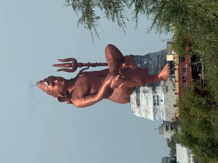 Enormous copper-coloured seated Shiva statue holding a trident rises above surrounding buildings.
