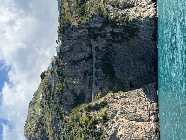Steep rocky cliff with arched coastal road above turquoise Mediterranean water