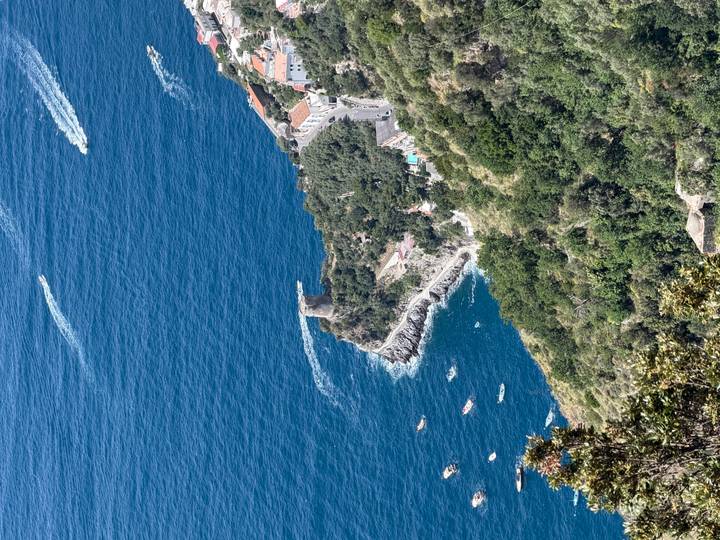 High aerial view of a coastal tower and village perched above deep blue sea with boat wakes
