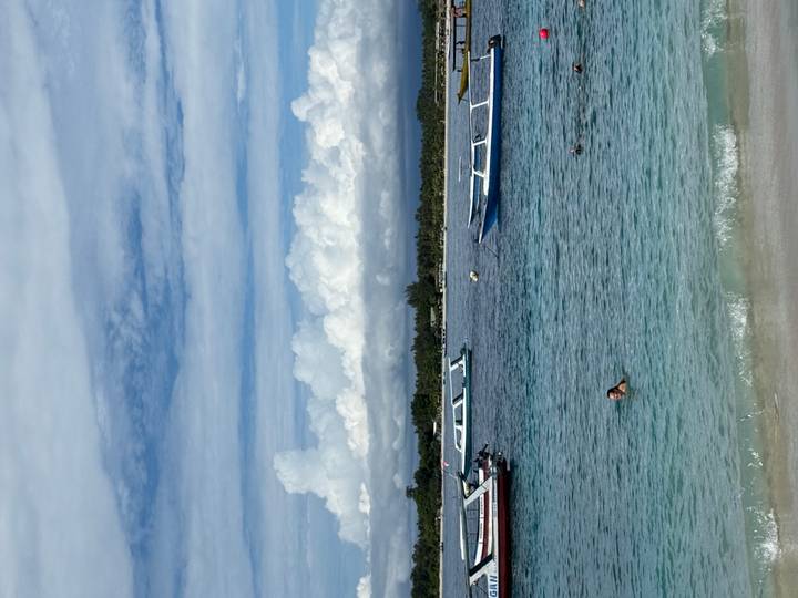 Turquoise sea with small boats anchored near a white-sand beach where a lone swimmer enjoys the water.