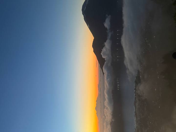 A vivid orange sunrise paints the sky above a sea of clouds and dark mountain silhouettes.