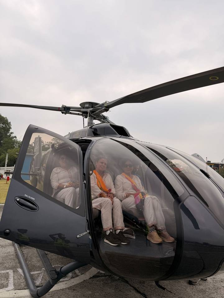 Three passengers dressed in white sit inside a sleek helicopter on a landing pad ready for takeoff.