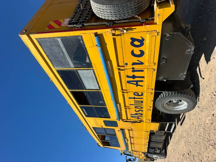 Bright yellow expedition truck labeled "Absolute Africa" parked on a dirt surface under clear blue sky.
