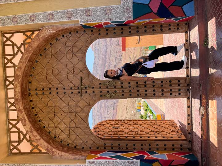 Traveller poses in ornate arched doorway with desert mountains visible beyond courtyard.