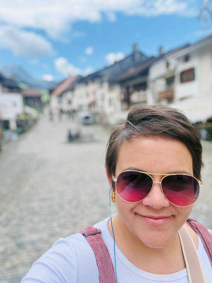 Close-up selfie of a traveler in sunglasses with a blurred cobblestone village street behind