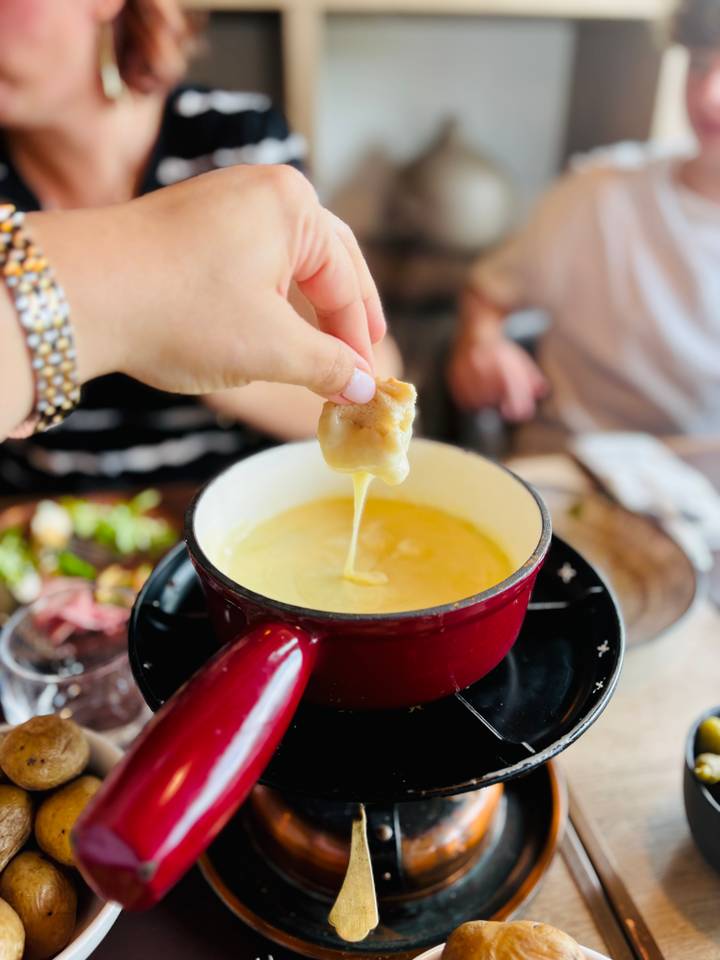 Hand dipping bread into creamy cheese fondue in a red pot