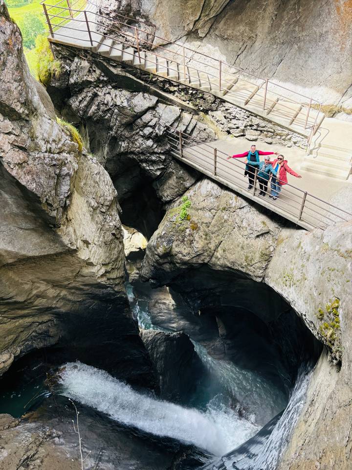 Travelers spread arms on a walkway above a deep rocky gorge with rushing water below