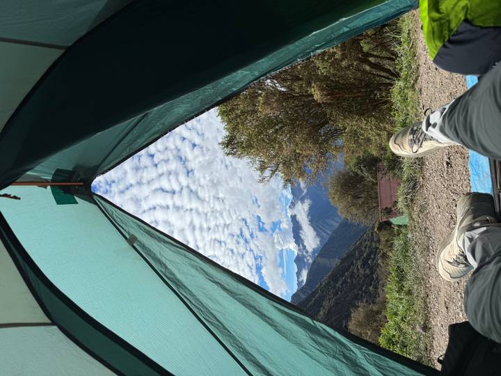 View from inside a tent of a cloud-streaked sky and distant Andes with trekkers’ feet in foreground