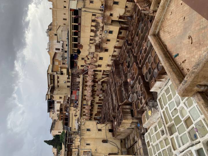 Elevated view over Fes tanneries showing hundreds of circular dye vats surrounded by aged buildings under an overcast sky.