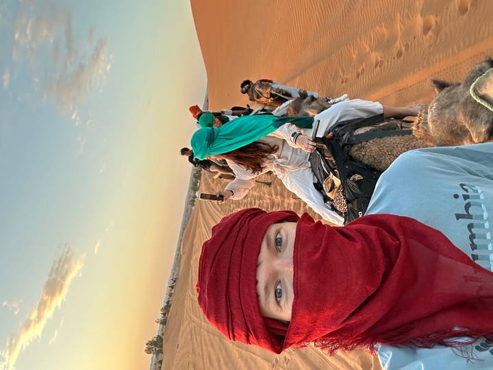 Selfie from camelback capturing fellow riders along golden sand ridges in the soft dawn light.
