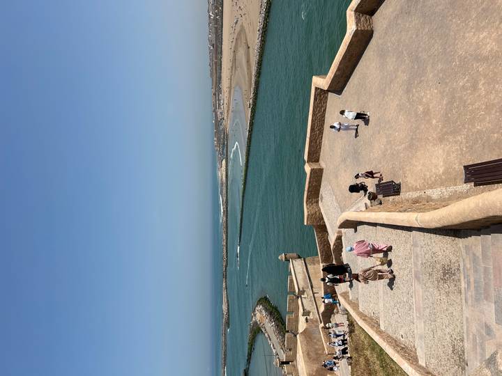 Panoramic view from ramparts over a turquoise river mouth and Atlantic coastline with visitors exploring the fort.
