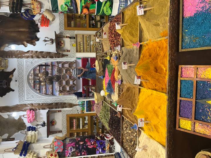 Colourful pyramids of ground spices and herbs fill a traditional Moroccan shop lined with bottles and jars.