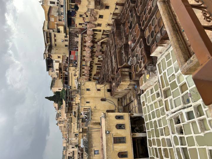 High viewpoint across the aged yellow walls and dye pits of Fes tannery under grey skies.