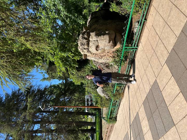 Traveller poses with a large stone lion sculpture in a leafy park.