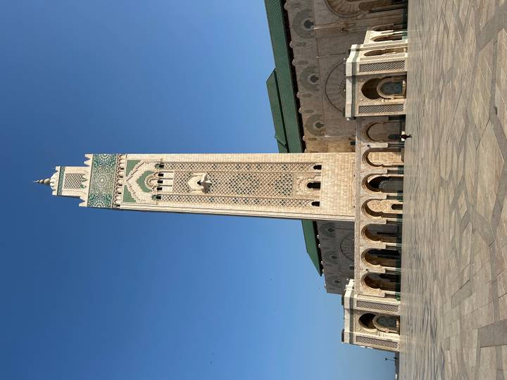 Tall minaret of Hassan II Mosque rises against a deep blue sky above vast stone plaza.