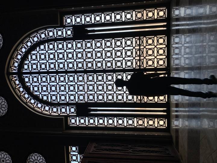 Silhouette of a visitor framed by ornate patterned iron doors inside Hassan II Mosque.