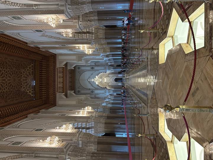 Grand interior hall of Hassan II Mosque adorned with chandeliers and intricate arches, visitors lining the nave.
