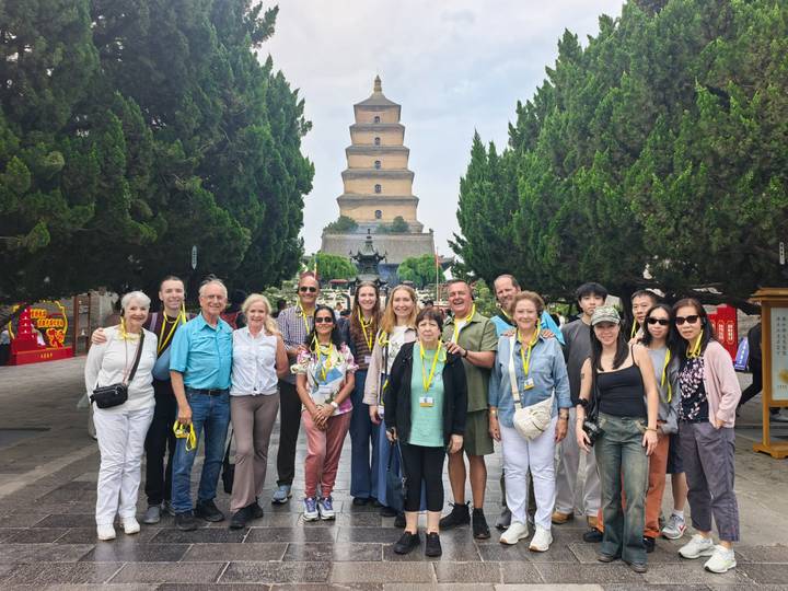 Tour group gathers in front of the multi-tiered Giant Wild Goose Pagoda framed by tall cypress trees.