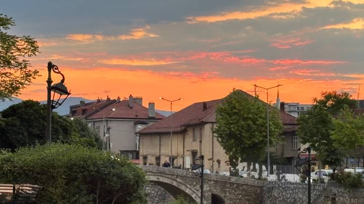 Warm sunset sky over historic Sarajevo rooftops and a small stone bridge in the foreground.