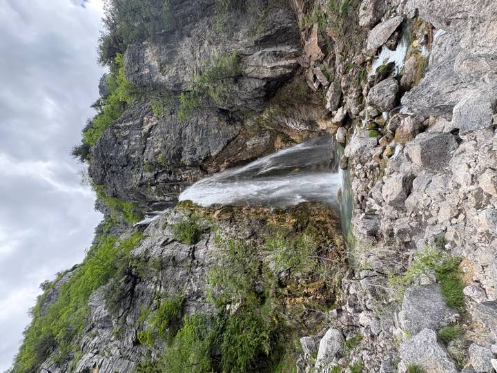 Tall waterfall cascading down rugged cliffs into a rocky pool in a mountain gorge.