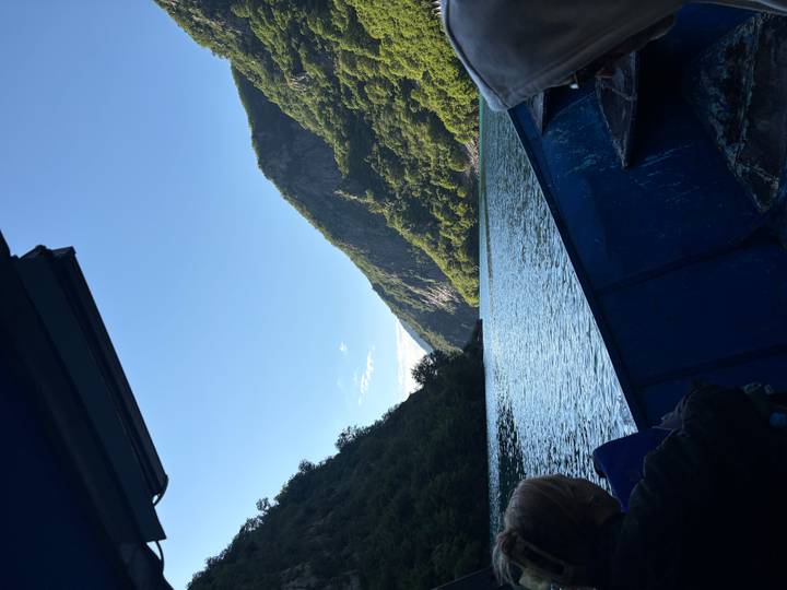 Boat gliding through the steep canyon walls of Lake Koman on a sunny morning.
