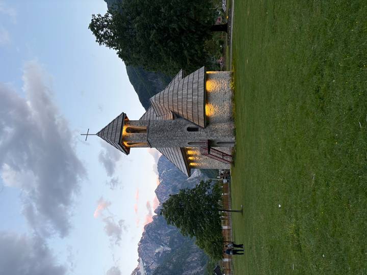 Stone Church of Theth lit warmly at dusk with mountain backdrop and grassy field.