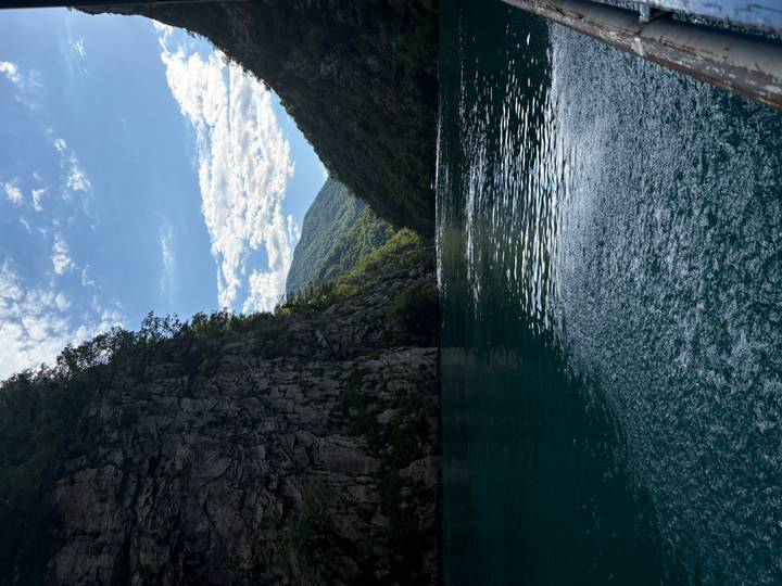Narrow turquoise gorge with towering rock faces and rippling water under a bright sky.