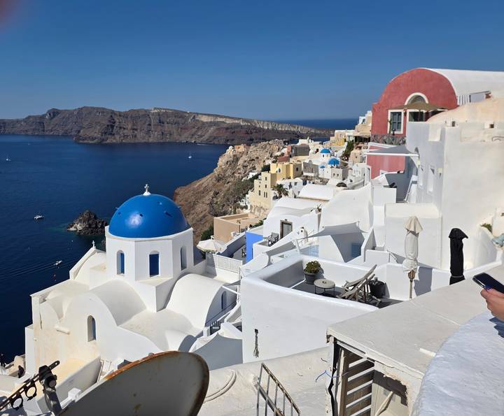 Classic Santorini scene of a blue-domed church and white Cycladic houses perched above the deep blue caldera.