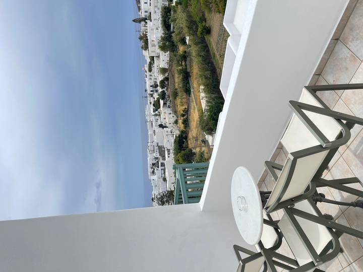 Balcony view over flat-roofed white village houses and fields under a moody sky.