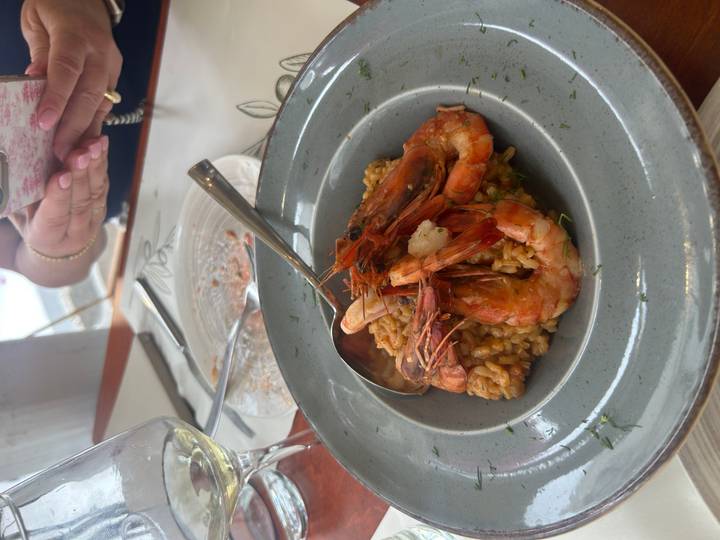 Risotto topped with grilled prawns served on a grey ceramic plate at a seaside taverna.