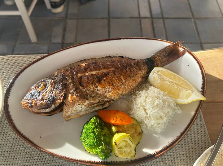 Grilled whole fish served with rice, lemon wedge and mixed vegetables on an oval plate.