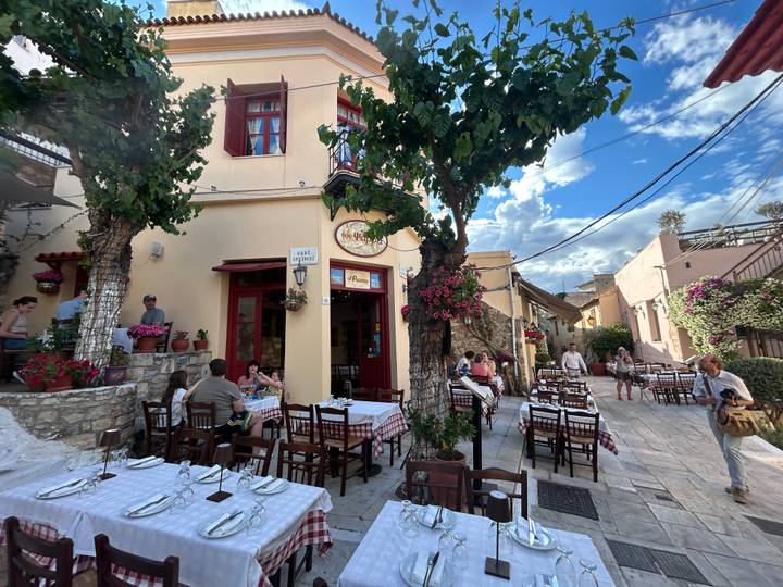 Charming Athens taverna with checked tablecloths, blooming bougainvillea and diners in a narrow stone lane.