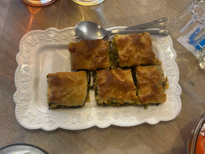 Tray of six pieces of Greek spanakopita with flaky golden crust served family-style.