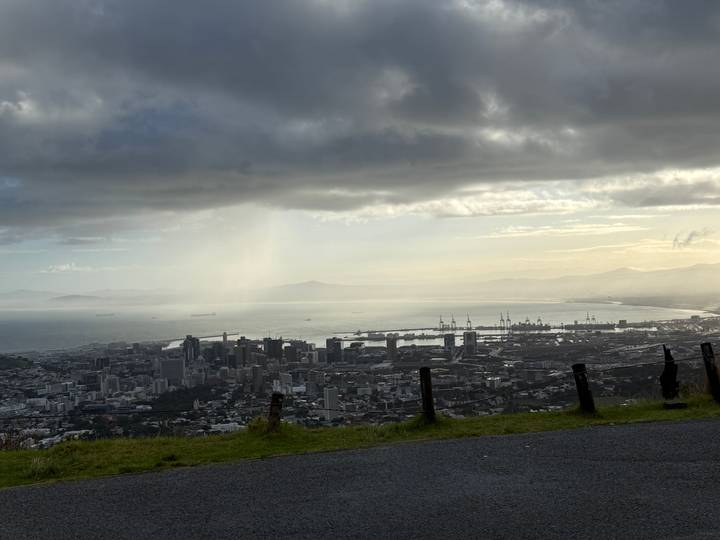 Moody panoramic view of Cape Town’s skyline and harbour from a mountain lookout beneath dramatic clouds and sunbeams.