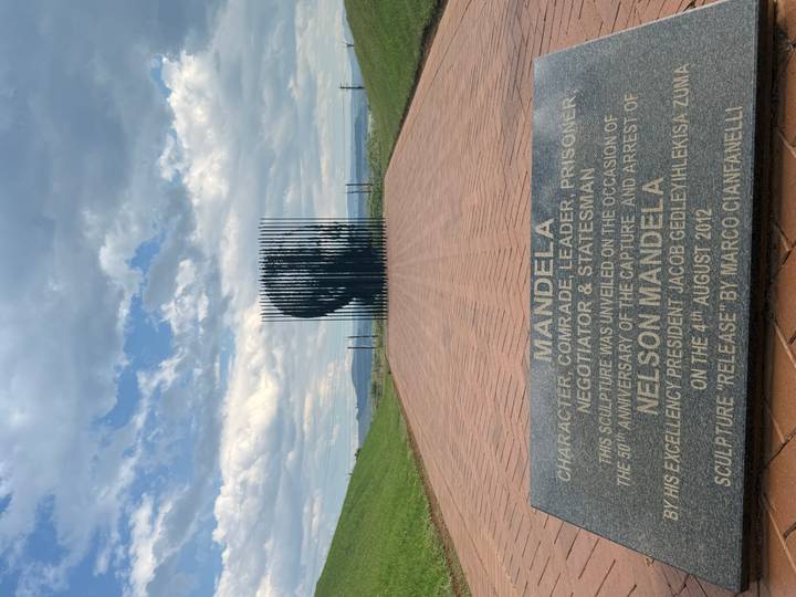 Perspective view of the Nelson Mandela Capture Site sculpture composed of vertical steel poles lining a brick walkway.