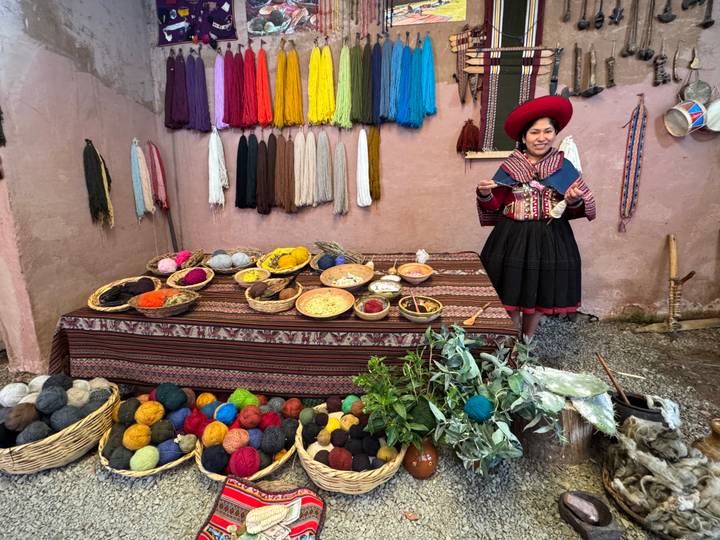 Andean woman in traditional dress demonstrating natural dyes and colourful yarns in a courtyard display.