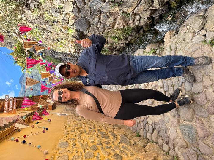 Two travellers smiling in a colourful cobblestone alley decorated with bright textiles and banners.