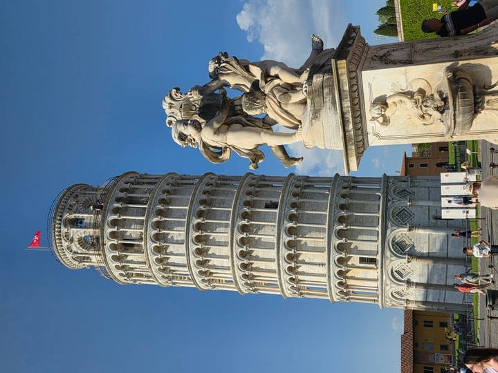 Iconic Leaning Tower of Pisa with marble statue in foreground against a clear blue sky.