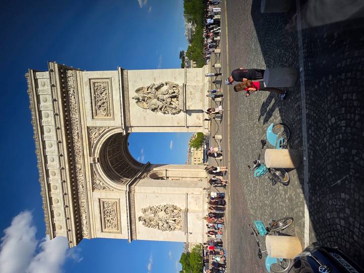 Crowds and cyclists gathered near the Arc de Triomphe on a sunny afternoon.