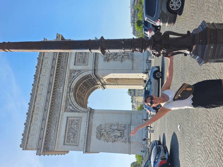 Woman joyfully posing in front of the Arc de Triomphe holding a lamppost.