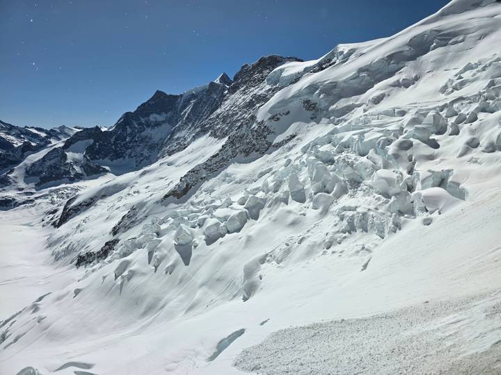 Expansive snowy alpine slope with jagged ice formations beneath towering peaks.